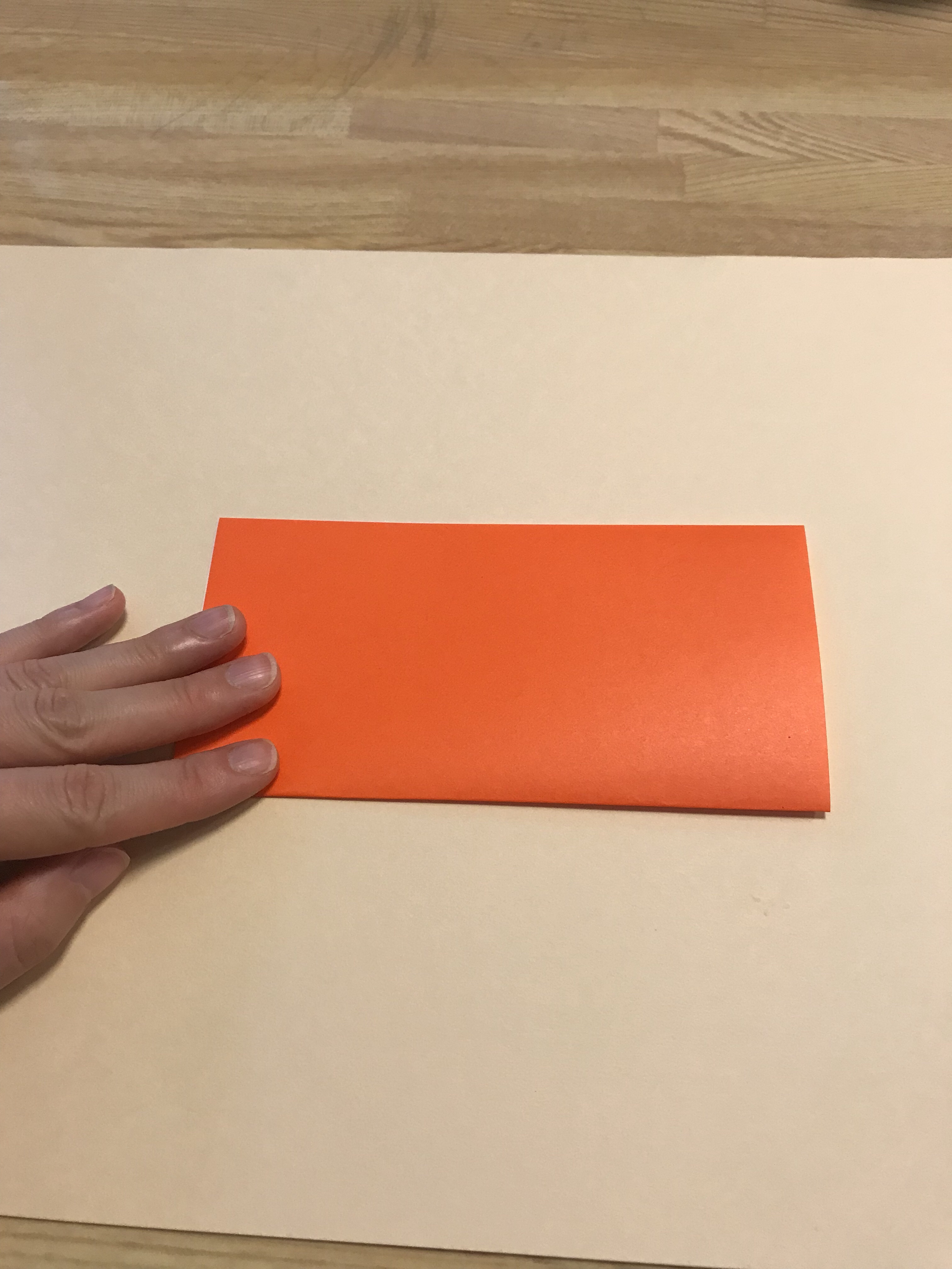 オレンジの折り紙を半分に折っている図